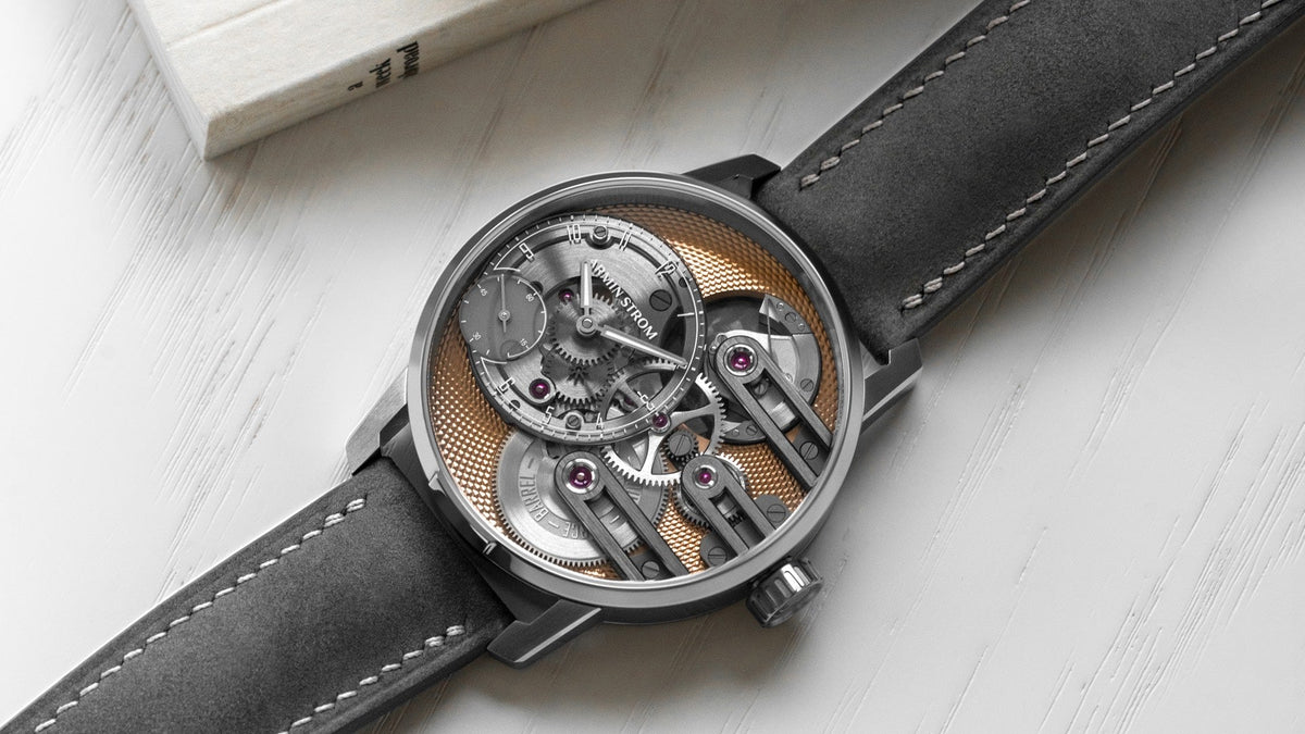 Armin Strom Gravity Equal Force resting beside a book, salmon guilloché mainplate and grey nubuck strap