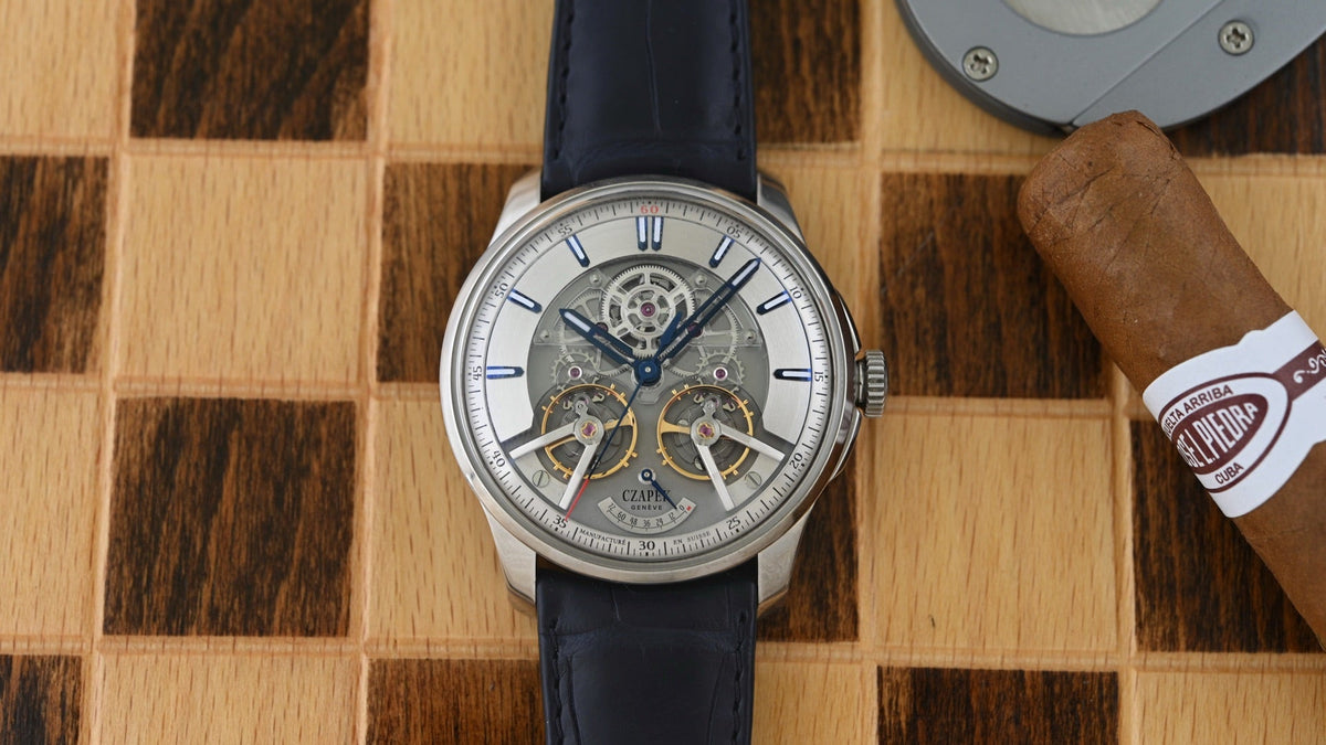 Czapek Place Vendôme Complicité Stardust Cobalt on a chessboard beside a cigar, open-worked dial with two balance wheels