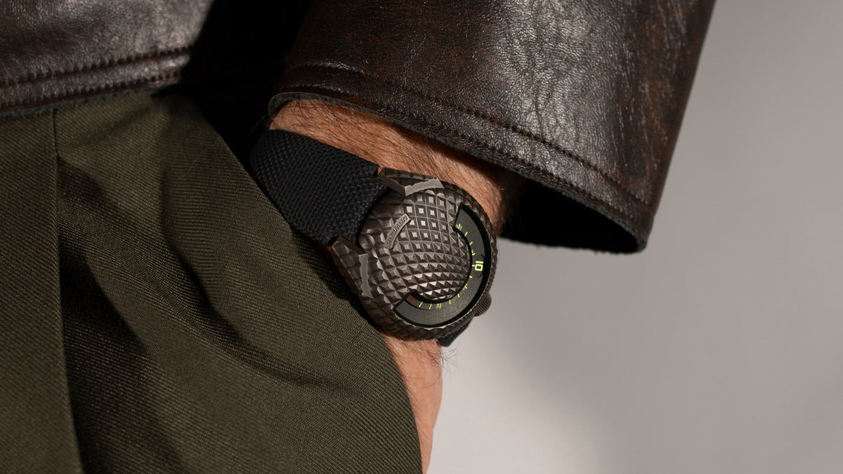 URWERK UR-101 T-Rex worn on the wrist, hand in a trouser pocket beneath a leather jacket cuff